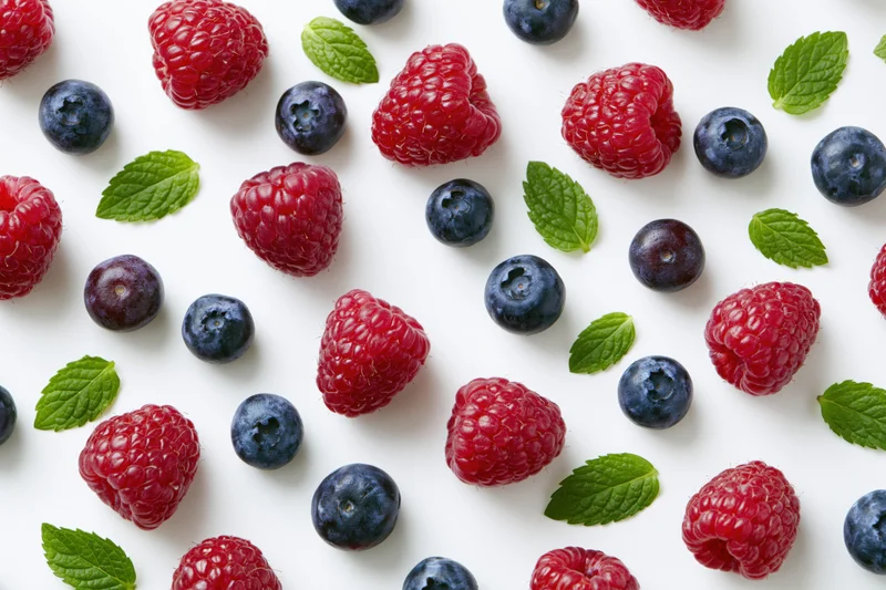 Raspberries and blueberries scattered with mint leaves on white surface
