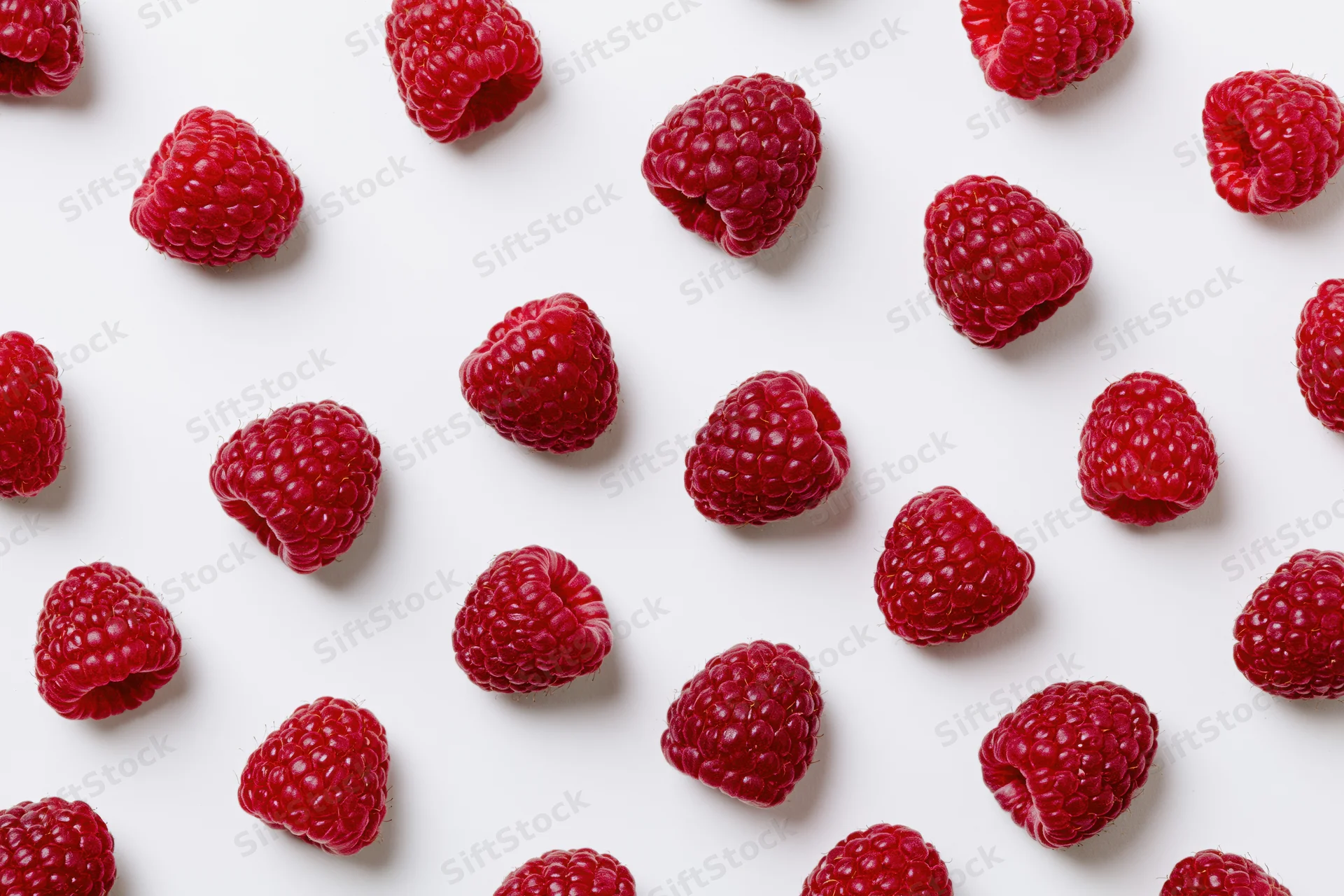 Fresh raspberries scattered across a white surface in a flat lay arrangement