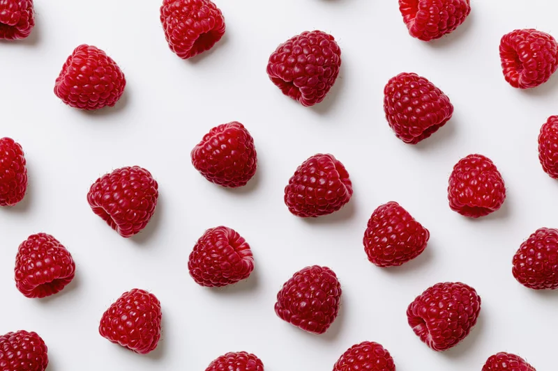 Fresh raspberries scattered across a white surface in a flat lay arrangement