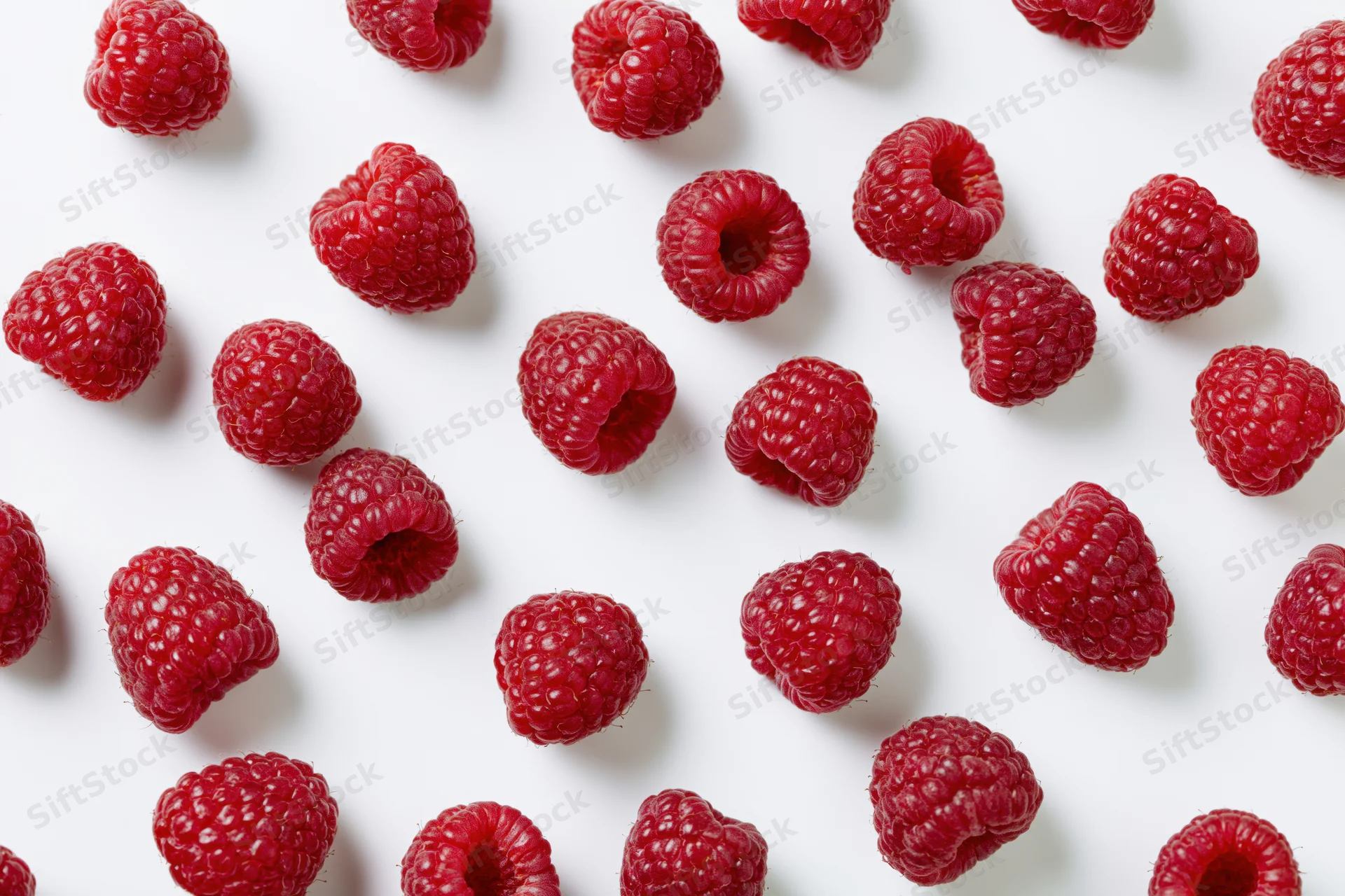 Fresh raspberries scattered across a white surface in a flat lay arrangement