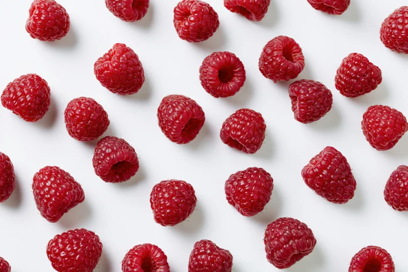 Fresh raspberries scattered across a white surface in a flat lay arrangement