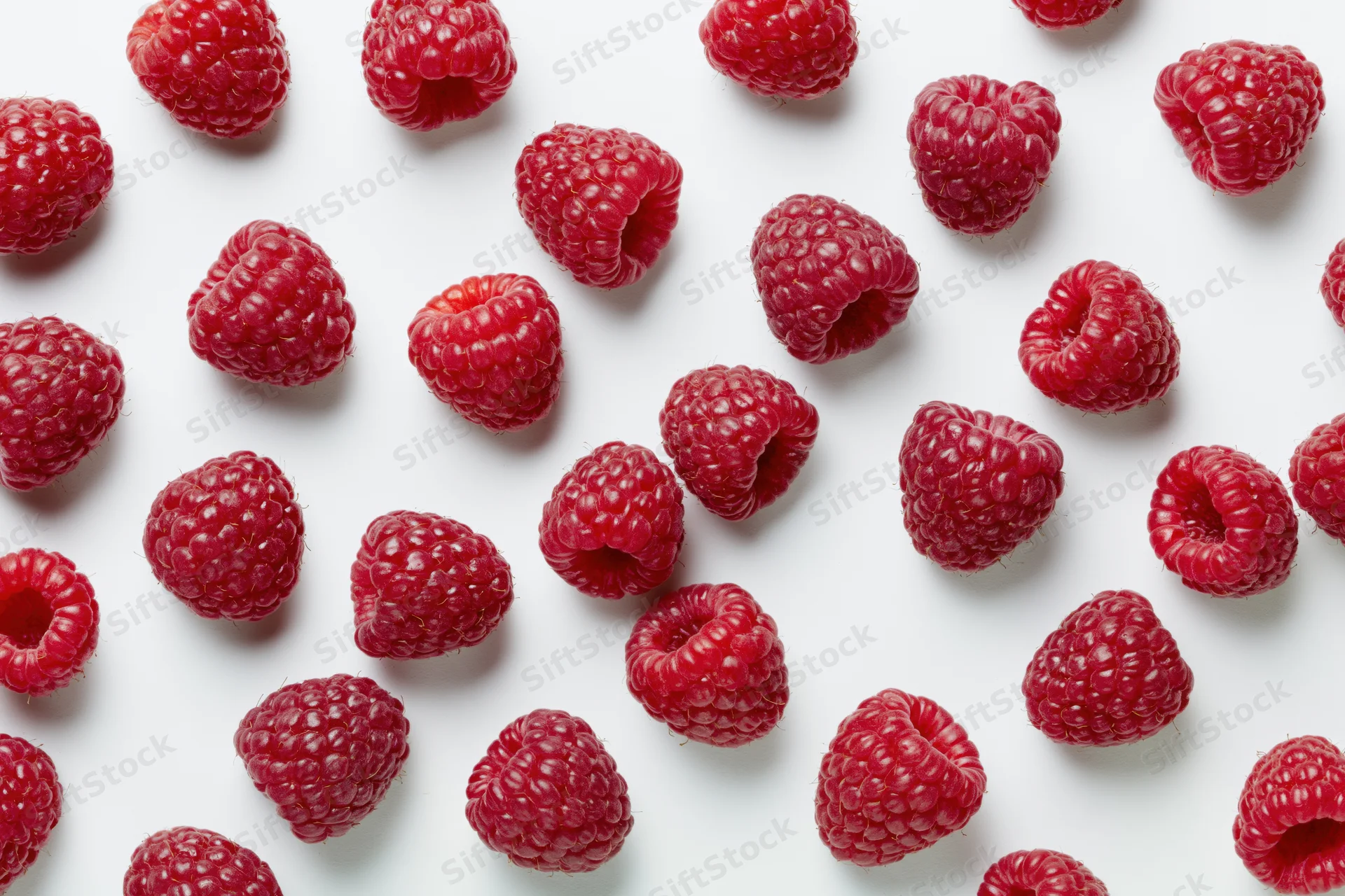Fresh raspberries scattered randomly across a pure white background
