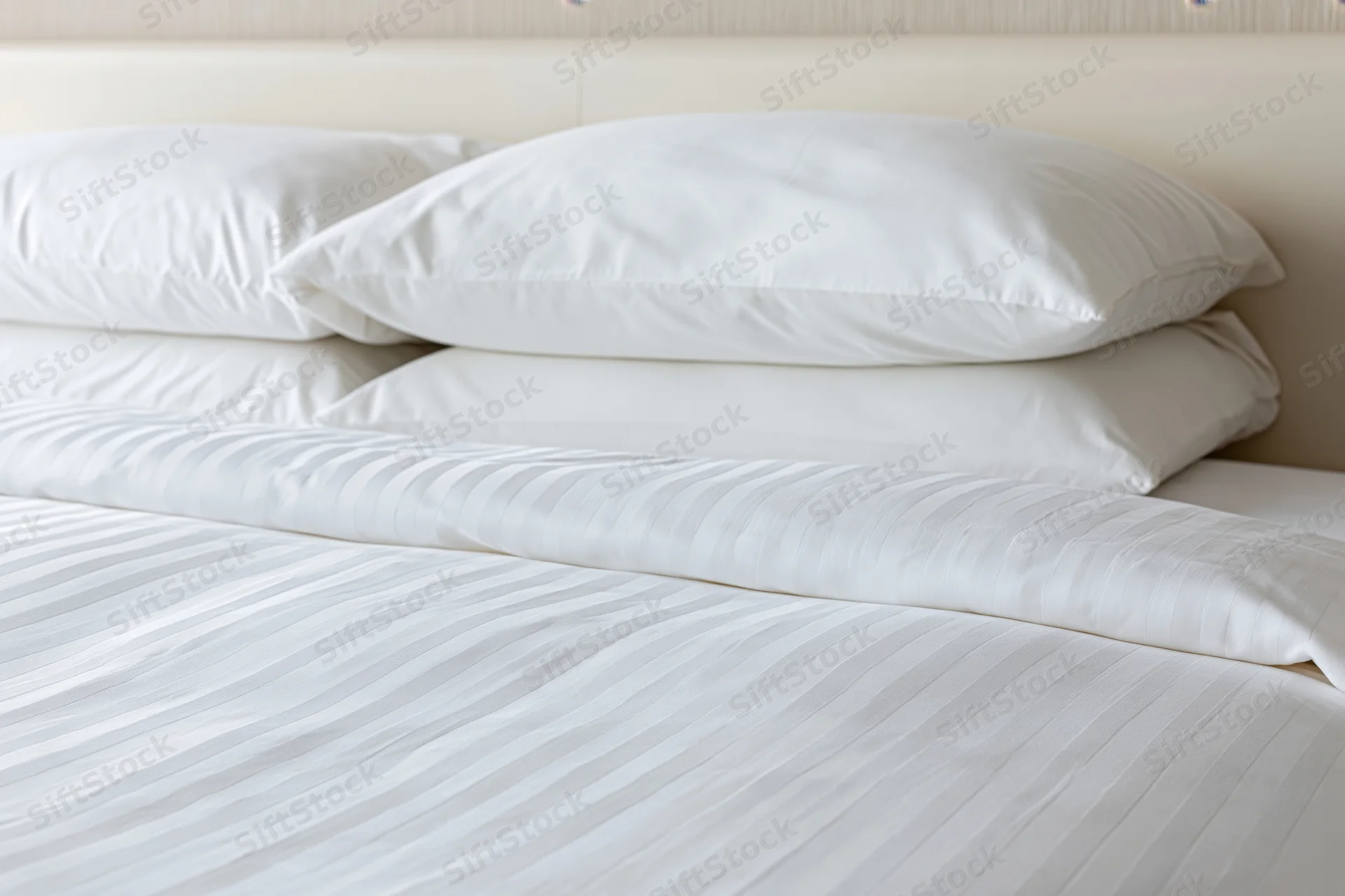 Freshly made hotel bed with three white pillows stacked against headboard, covered in striped sheets and duvet