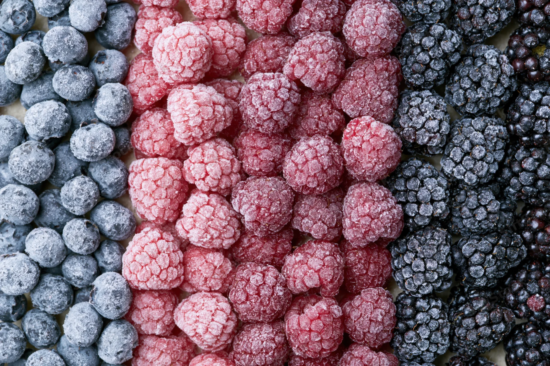Frozen mixed berries arranged in vertical stripes of blueberries, raspberries and blackberries filling the frame