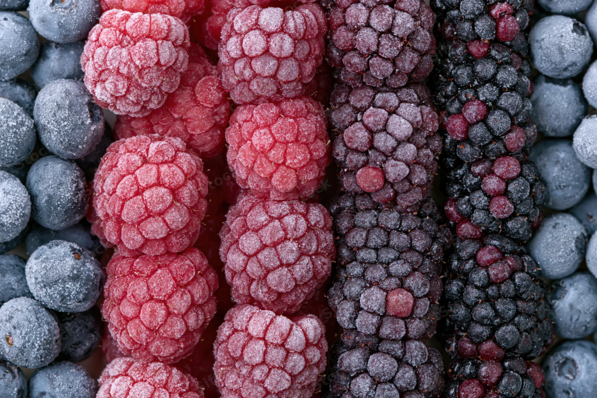 Frozen mixed berries arranged in vertical rows of raspberries, blueberries and blackberries filling the frame