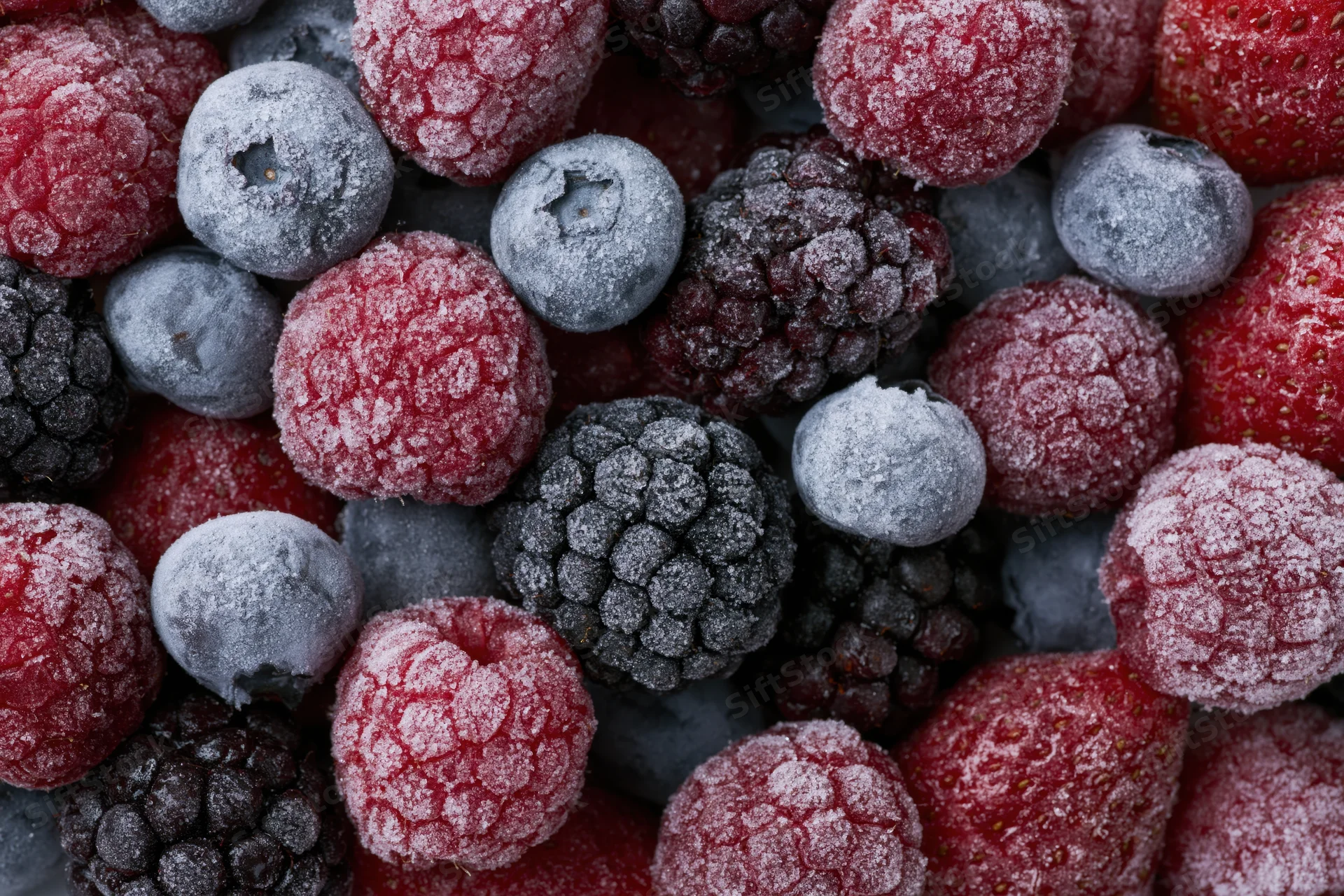 Frozen mixed berries covered in frost, close-up view of raspberries, blueberries, and blackberries