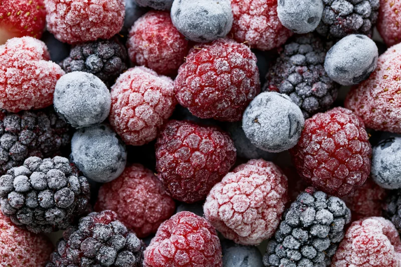 Closeup of frozen mixed berries covered in frost, including raspberries, blueberries and blackberries
