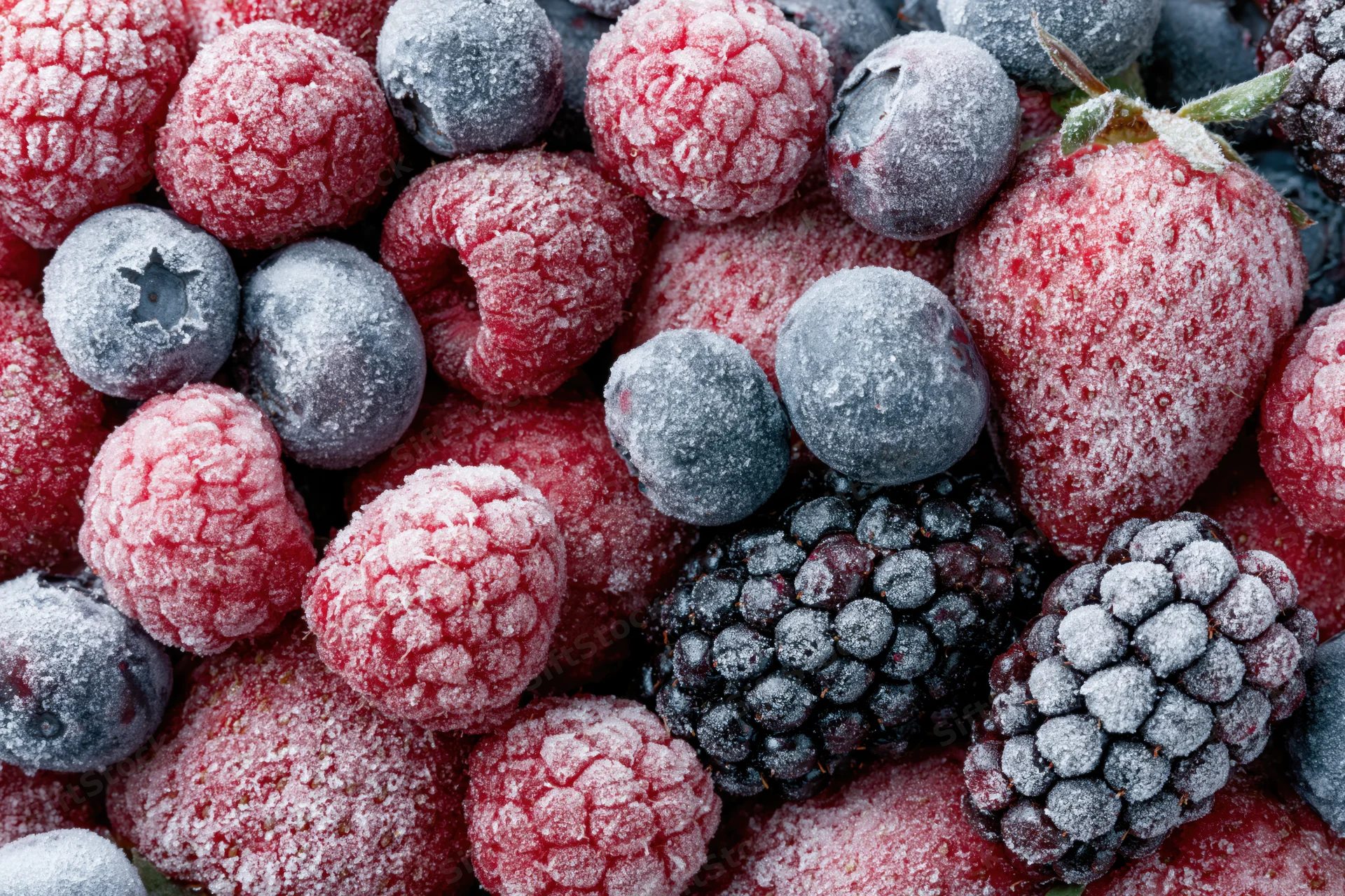 Closeup of frozen mixed berries including raspberries, blueberries, blackberries and strawberries covered in frost