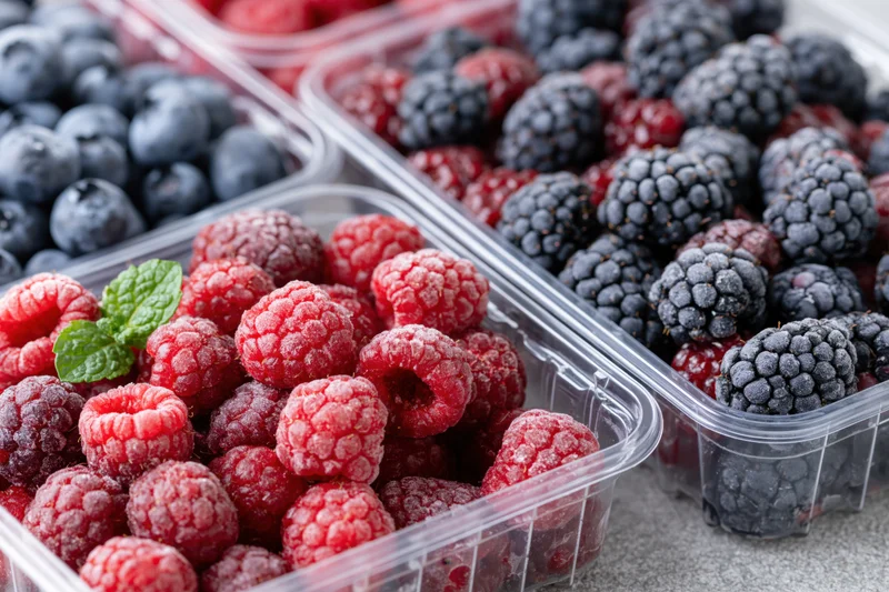 Frozen raspberries blueberries and blackberries in clear plastic containers on a gray countertop