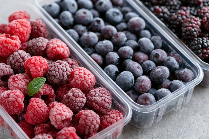Frozen raspberries blueberries and blackberries in clear plastic containers on a countertop