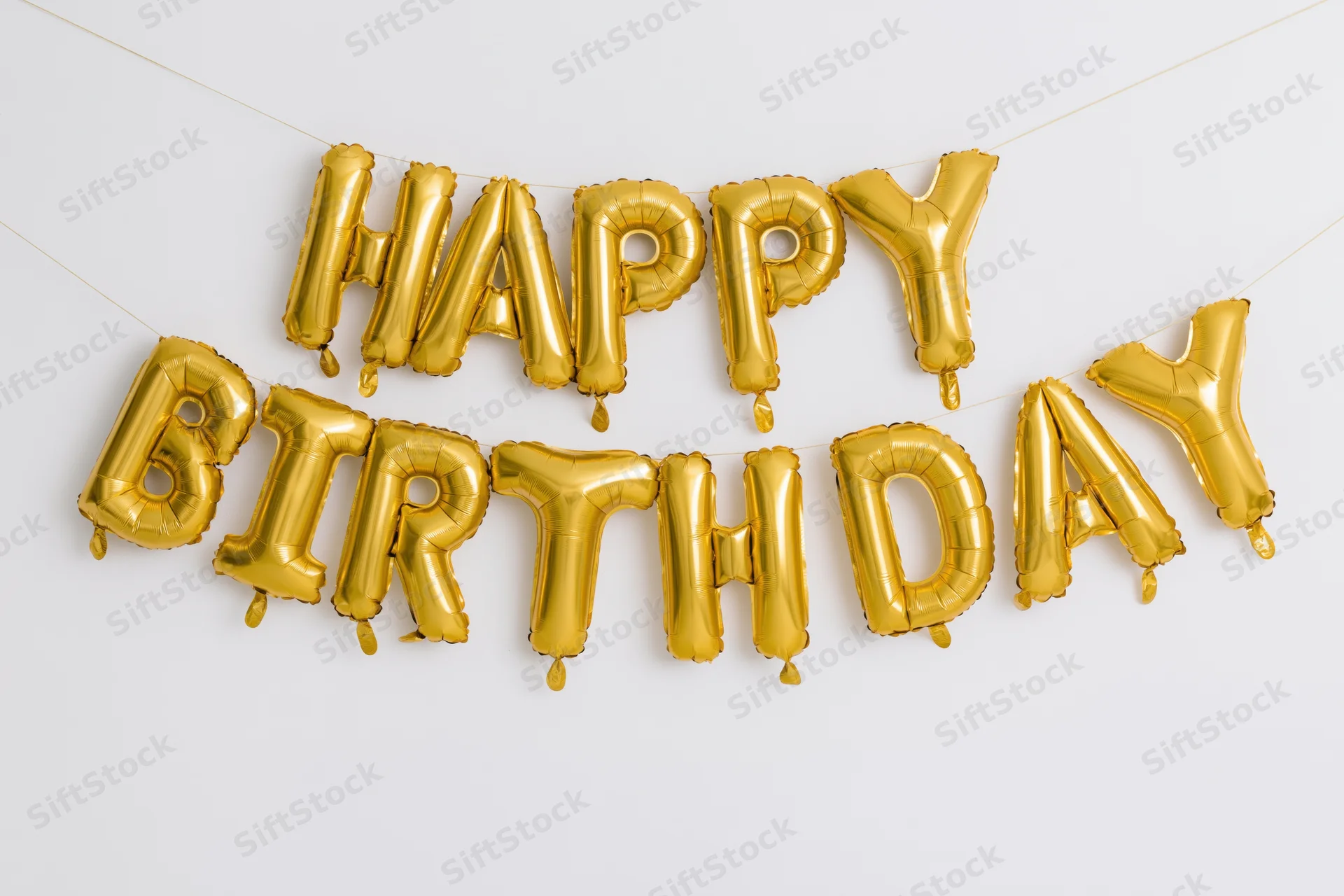 Gold foil letter balloons spelling happy birthday on a white wall