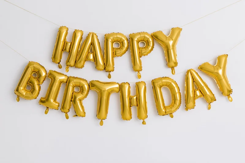 Gold foil letter balloons spelling happy birthday on a white wall