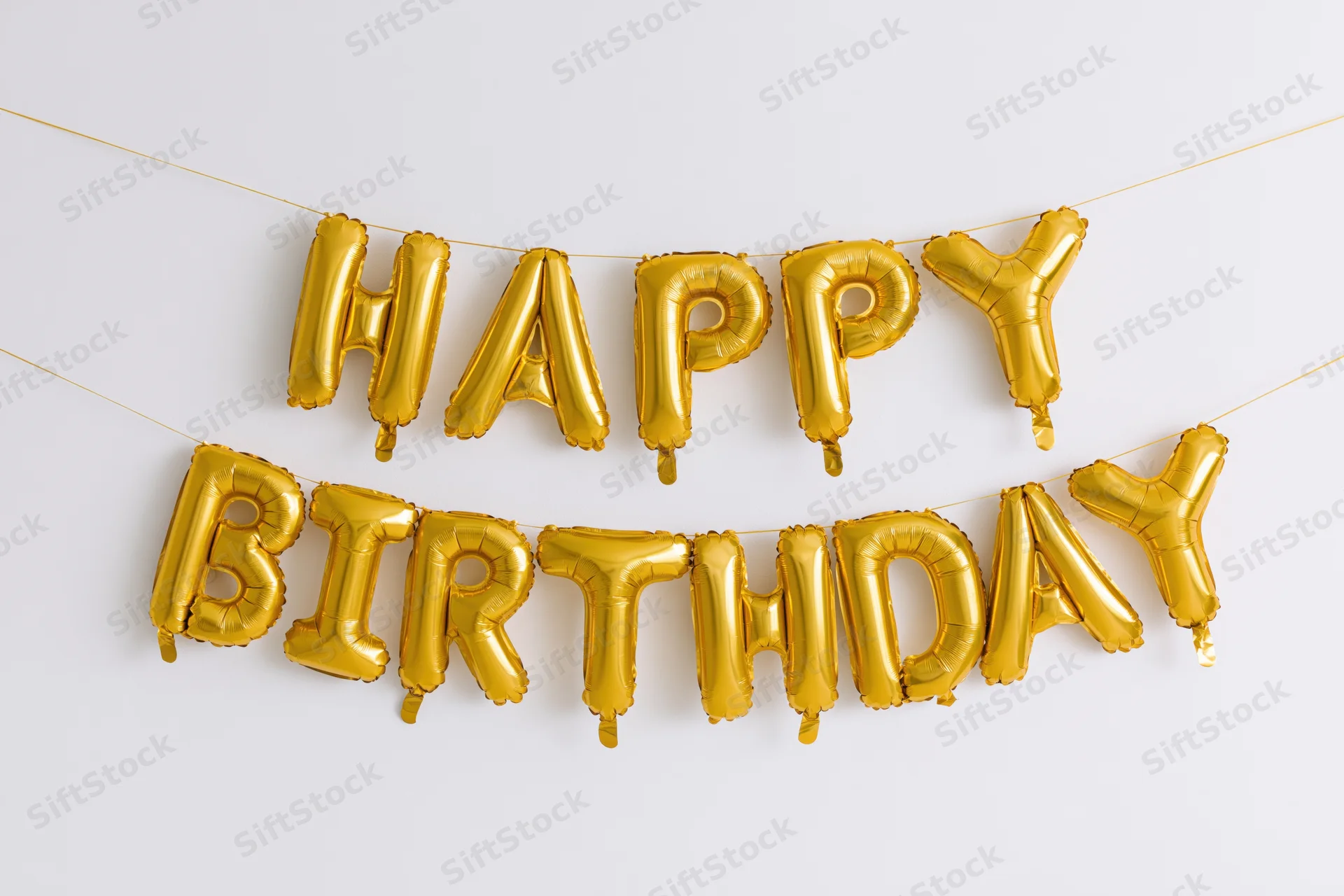 Gold foil letter balloons spelling happy birthday in two rows on a white background