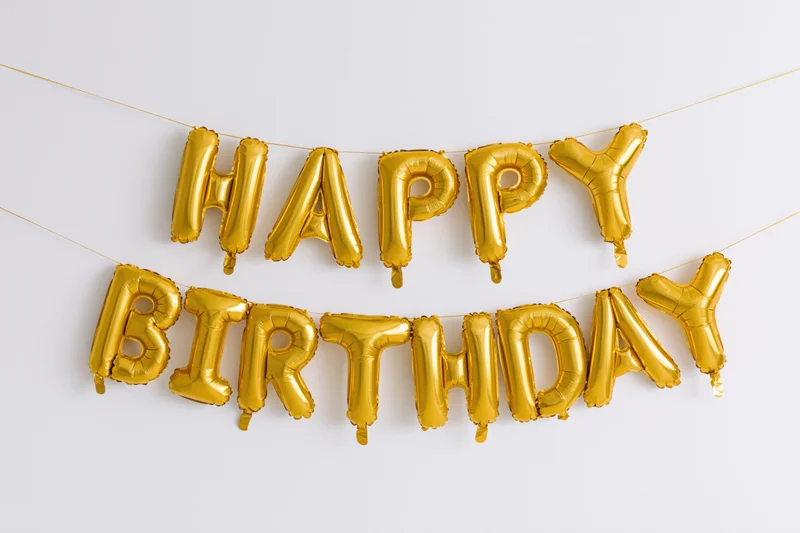 Gold foil letter balloons spelling happy birthday in two rows on a white background