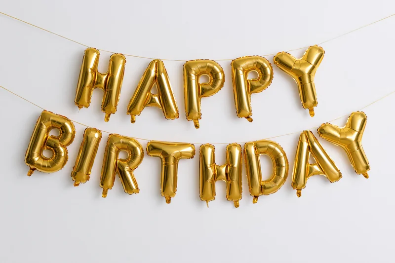 Gold foil letter balloons spelling happy birthday in two rows on a white wall