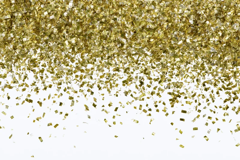 Gold metallic confetti pieces falling and scattering mid-air against white background