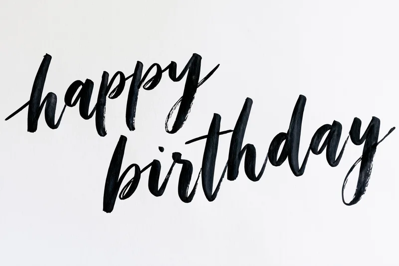 Hand-lettered happy birthday text in black brush calligraphy on white background