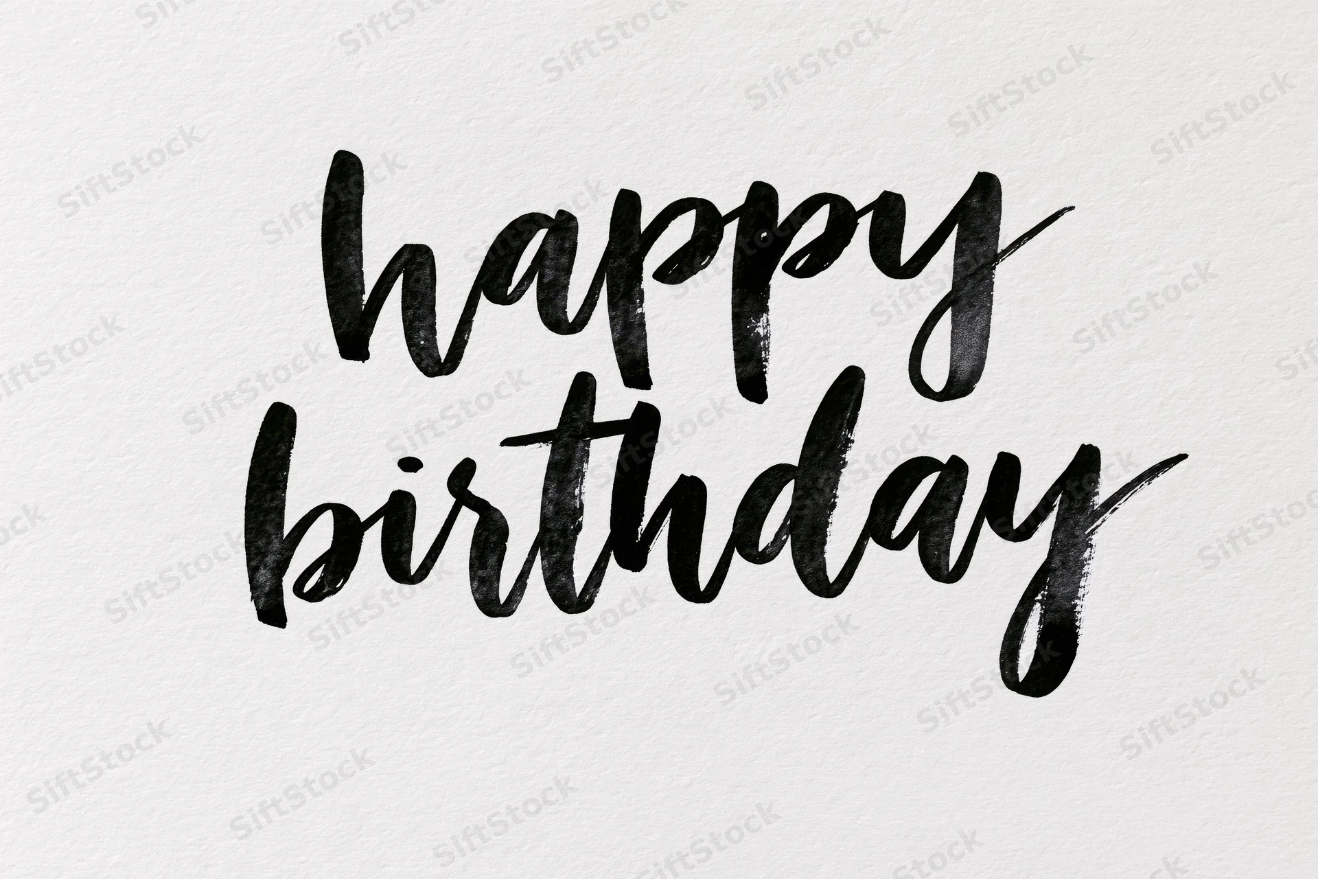 Hand-lettered happy birthday text in brush calligraphy on textured white paper