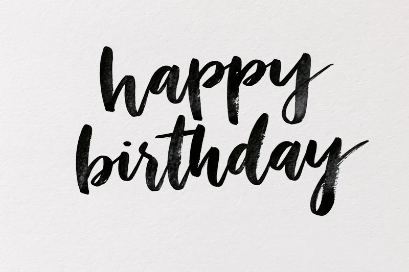 Hand-lettered happy birthday text in brush calligraphy on textured white paper
