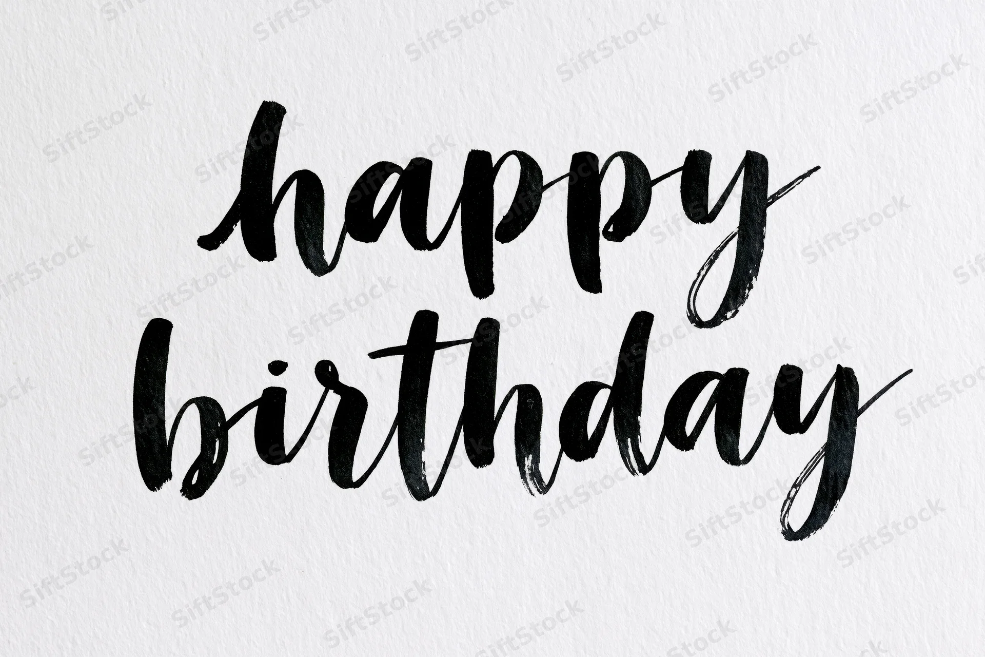 Hand-lettered happy birthday brush calligraphy on textured white paper