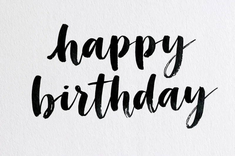 Hand-lettered happy birthday brush calligraphy on textured white paper