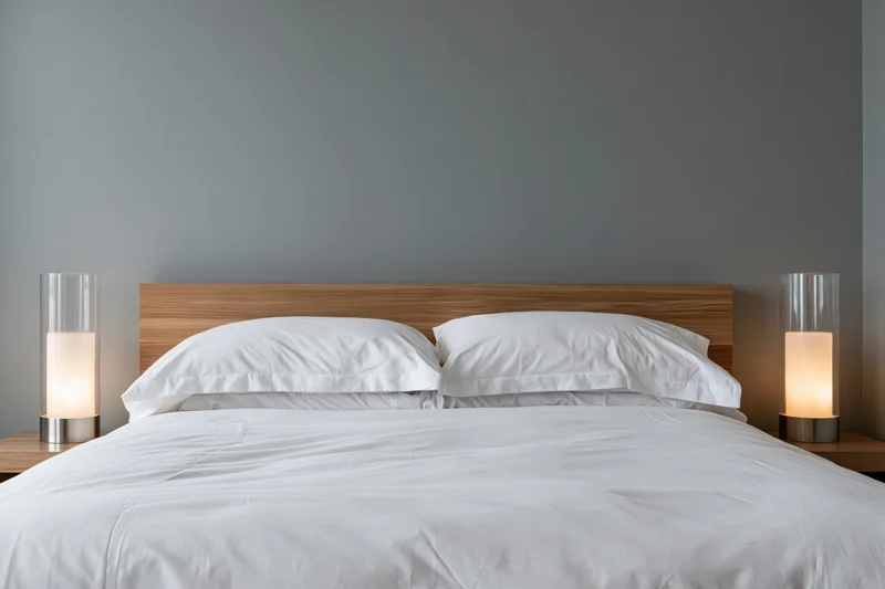 Hotel bed with white pillows on a modern wooden headboard flanked by lamps on nightstands
