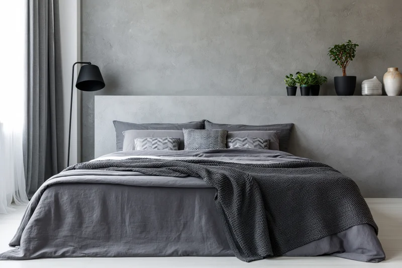 Industrial-style bedroom with king-size bed dressed in gray bedding against concrete wall