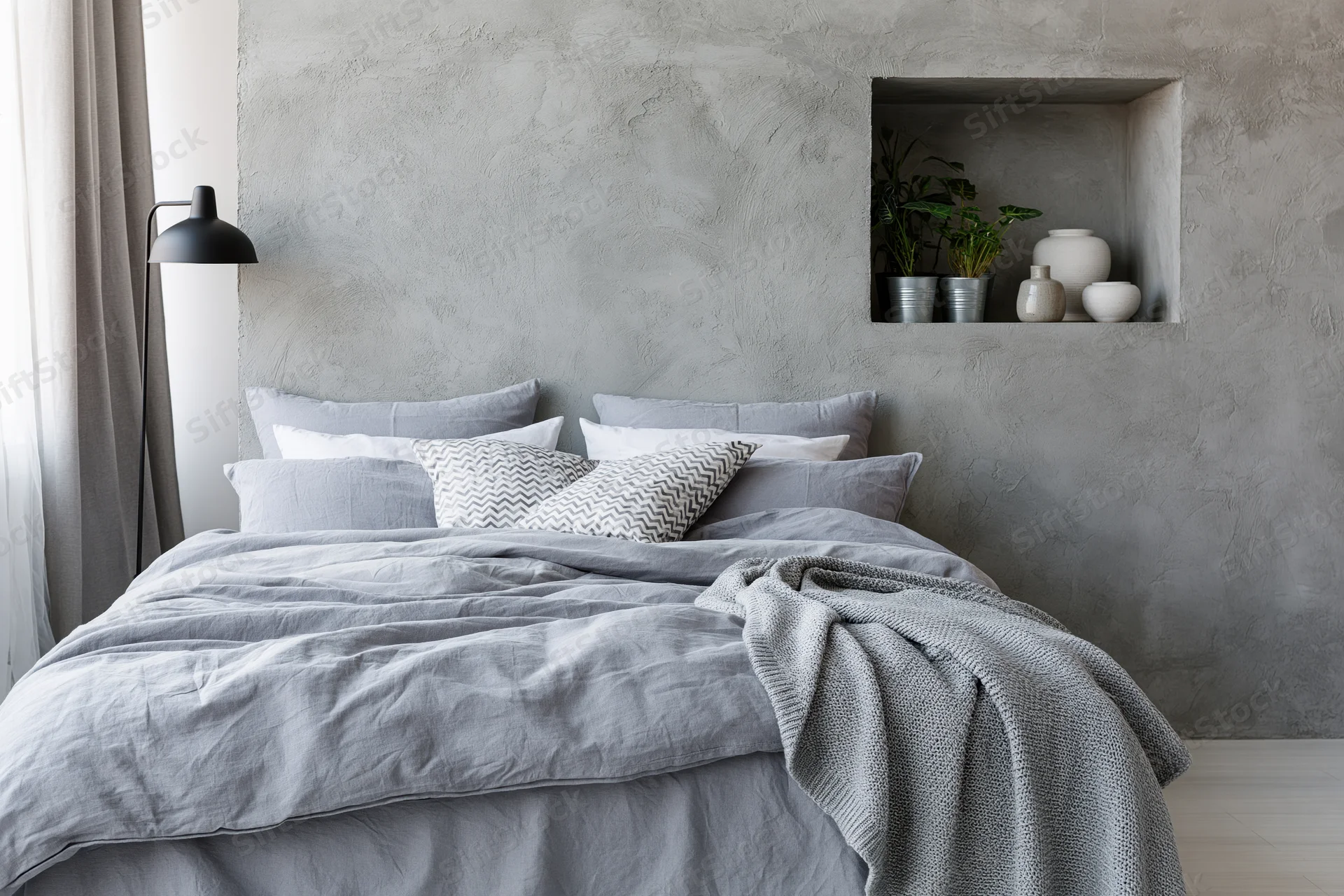King-size bed with gray bedding and concrete wall in industrial-style bedroom