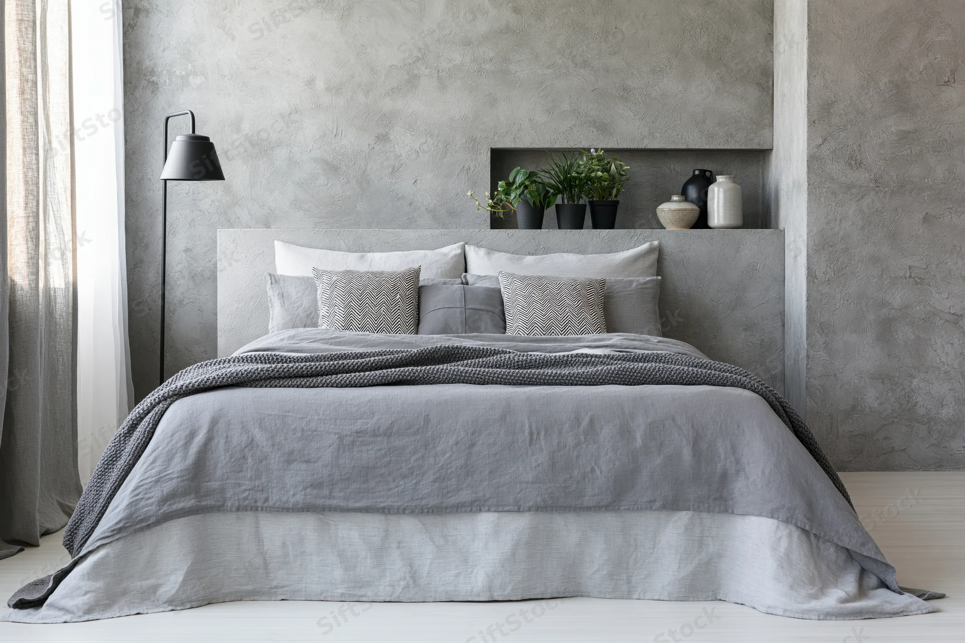 King-size bed with gray bedding and concrete headboard in industrial bedroom interior