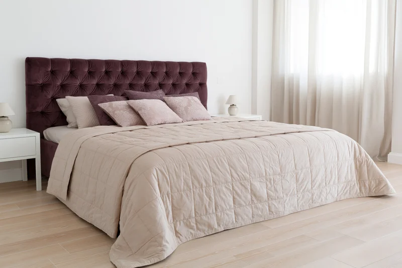 King-size bed with tufted dark mauve velvet headboard and beige bedding in a modern bedroom