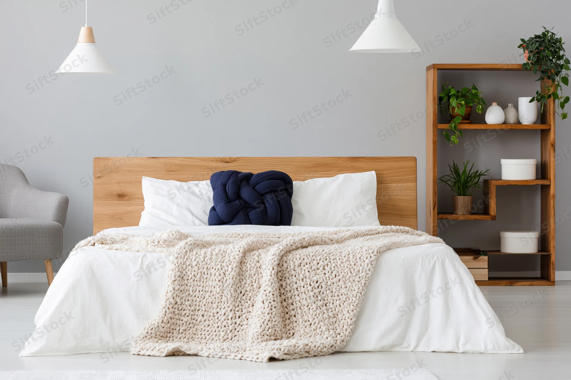 Minimalist bedroom with wooden bed and white bedding, featuring knit throw and shelving unit with plants
