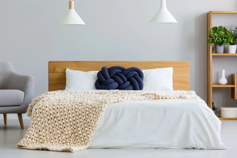 Minimalist scandinavian bedroom with wooden headboard, white bedding, knitted blanket, and pendant lamps