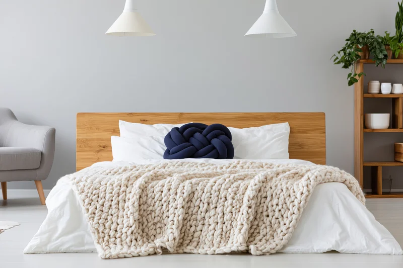 Minimalist scandinavian bedroom with wooden headboard, white bedding, chunky knit blanket, and pendant lamps