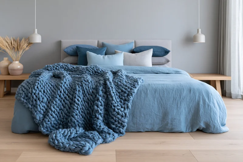 Queen bed with blue knit blanket and pillows in minimalist scandinavian bedroom