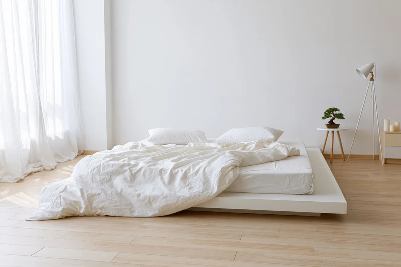 Minimalist bedroom with low platform bed and white bedding near a window with sheer curtains