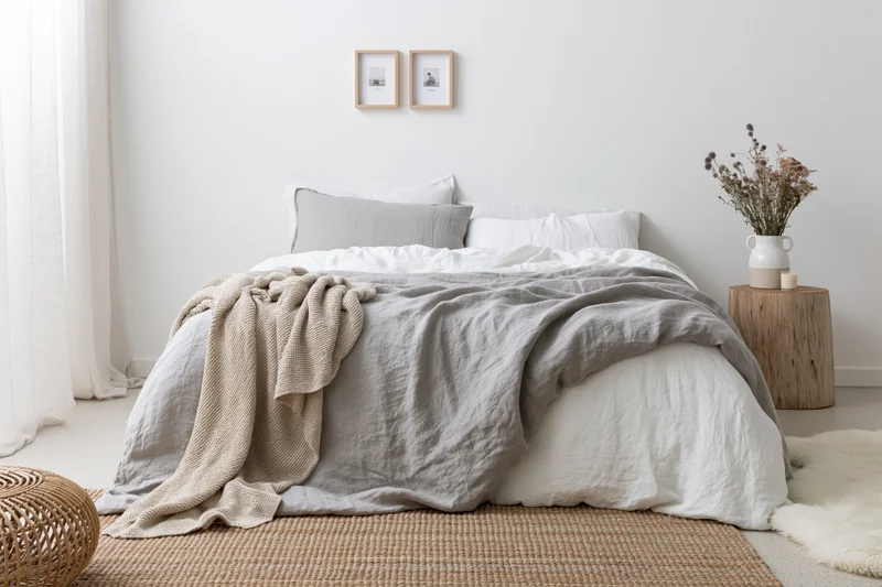 Double bed with layered gray and white bedding in minimalist bedroom interior