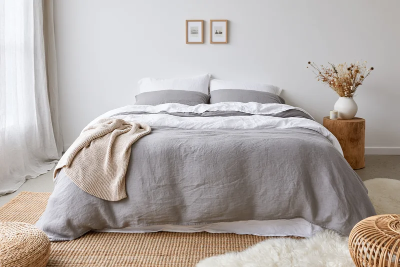 Double bed with layered gray and white bedding in a minimalist bedroom with natural materials and decor