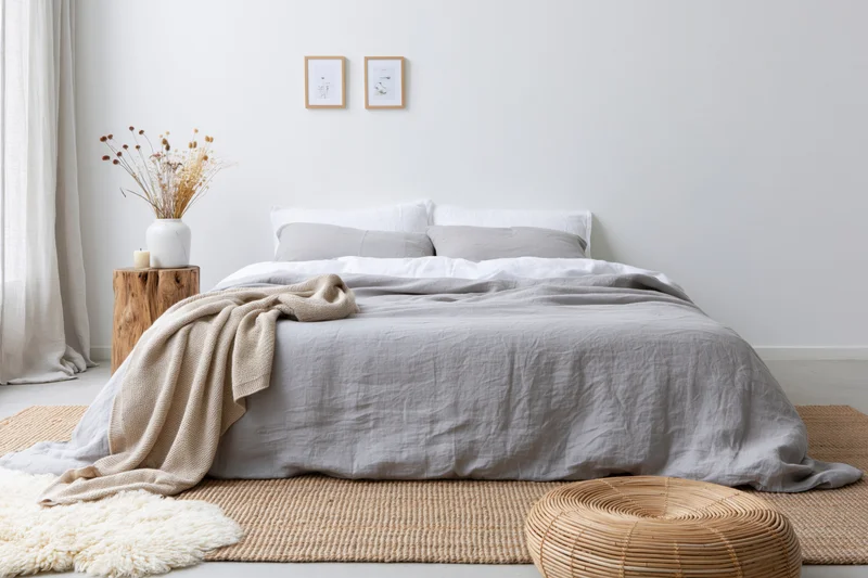 Double bed with gray linen bedding and neutral decor in a minimalist bedroom