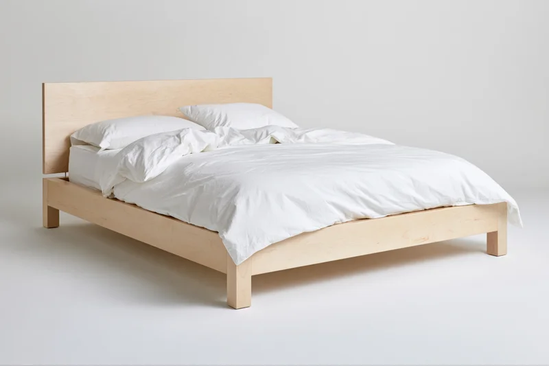 Minimalist platform bed with pale birch wood frame and white bedding in a clean studio setting