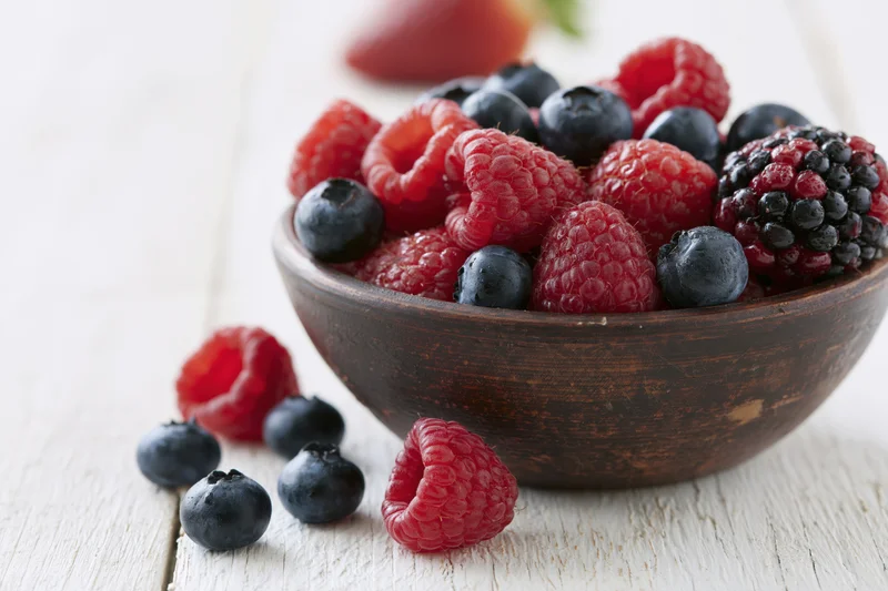 Mixed berries in a wooden bowl on a white wooden surface