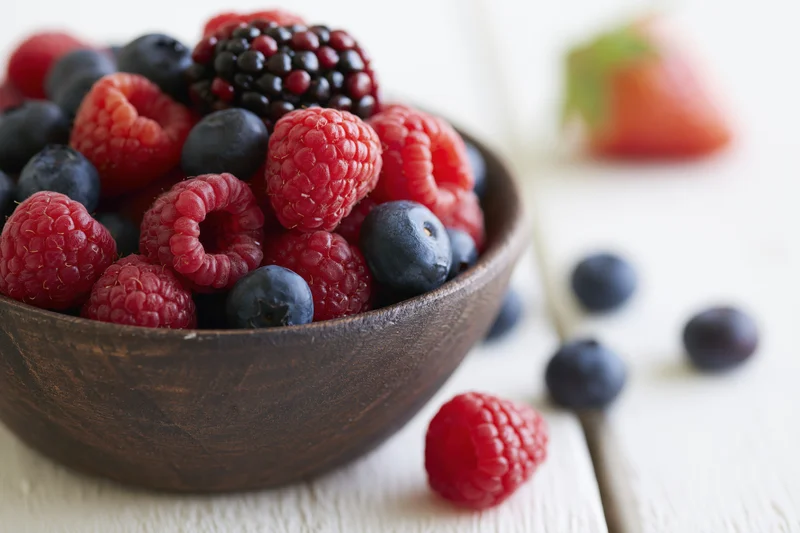 Mixed berries in a wooden bowl on a white surface