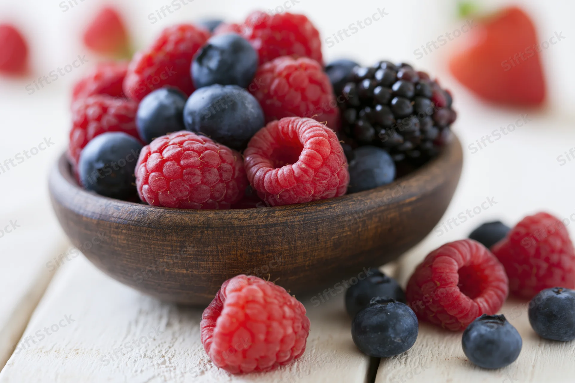 Mixed berries in a wooden bowl on a white wooden surface