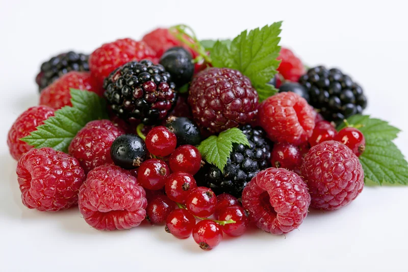 Mixed fresh berries piled together with green leaves on white background