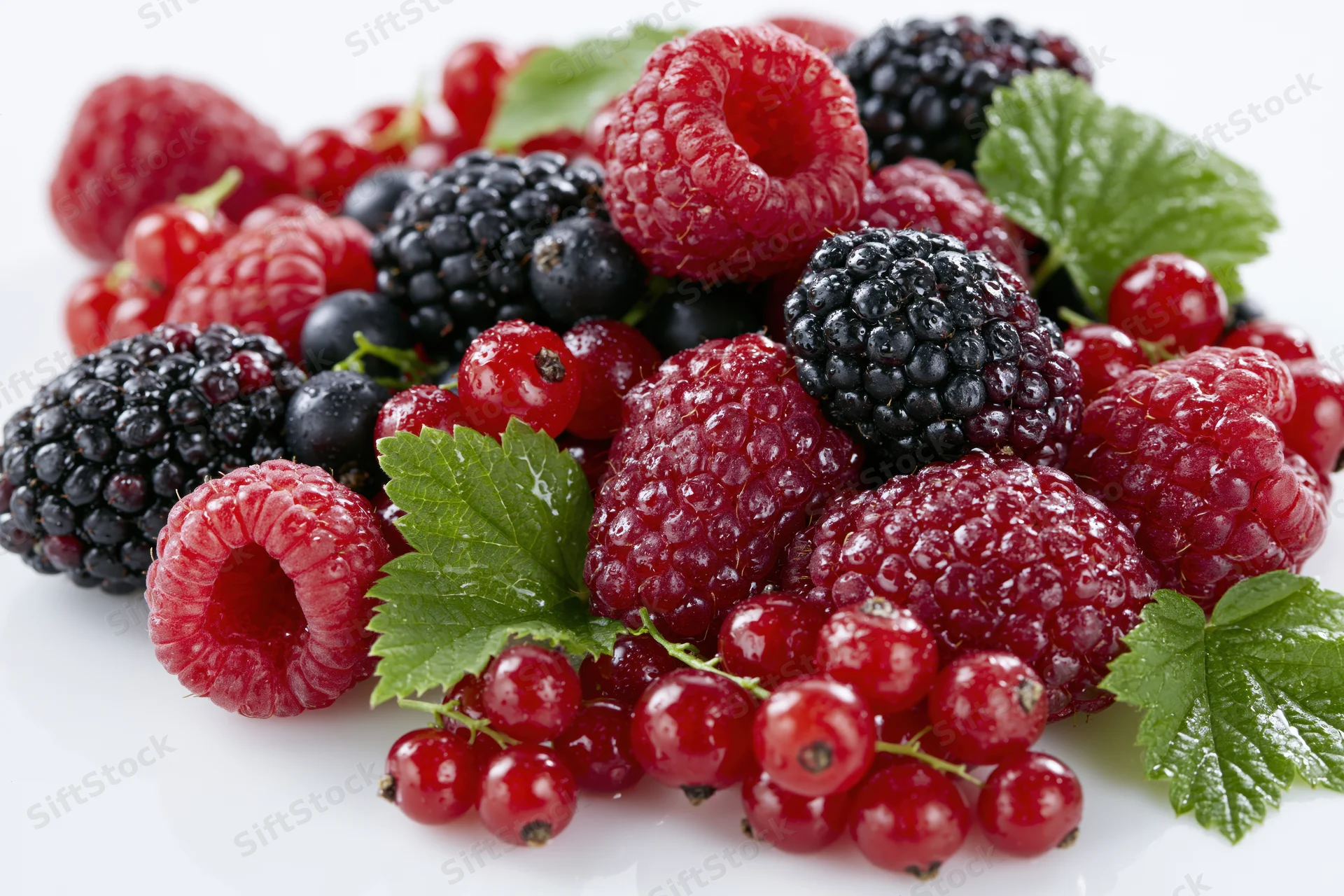 Mixed fresh berries piled together with green leaves on a white surface