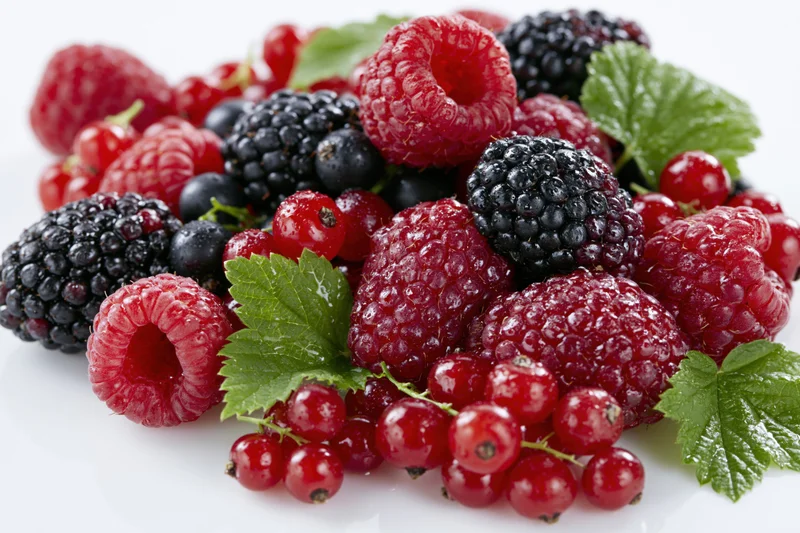 Mixed fresh berries piled together with green leaves on a white surface