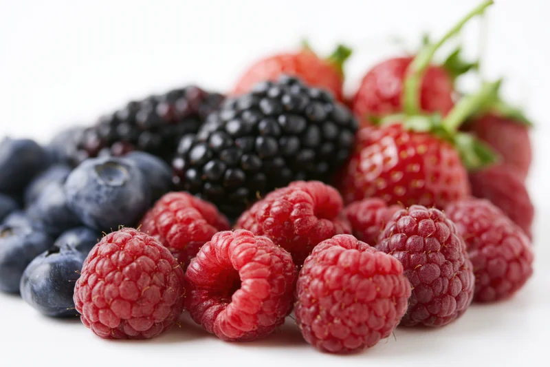 Mixed fresh berries piled together on a white surface