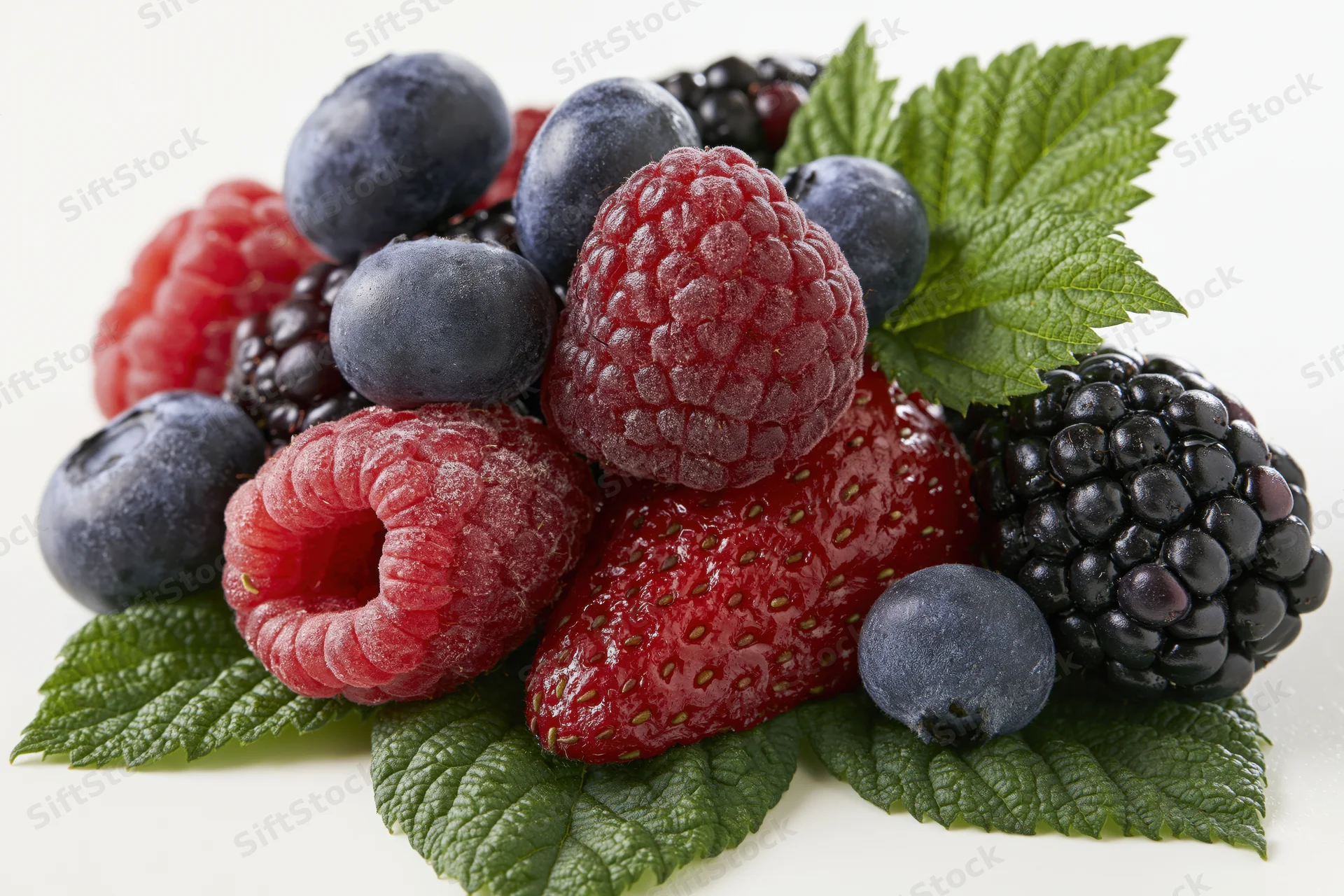 Mixed fresh berries piled on green leaves against white background