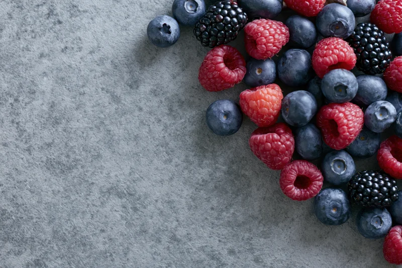 Mixed fresh berries arranged on a gray stone surface with copyspace on the left