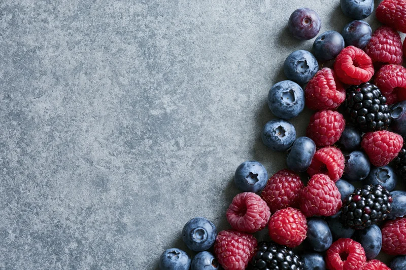 Mixed fresh berries arranged in corner on gray stone surface with copyspace