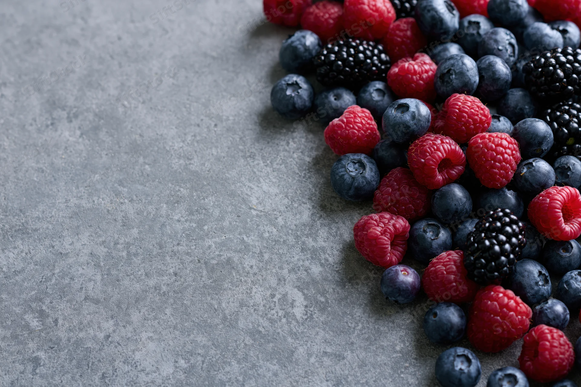 Mixed fresh berries arranged in corner on gray stone surface